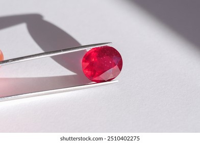 Lead glass filled natural ruby gemstone in tweezers. Heated, treated, affordable red gemstone. Mass market ruby gemstone mined in Madagascar, faceted in Thailand. Bright red colored gemstone setting.