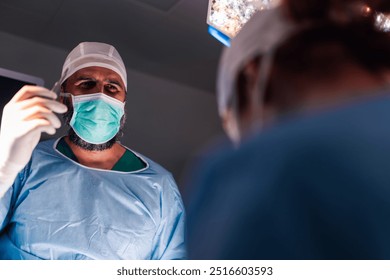 A lead surgeon in a modern operating room discusses procedures with other surgeons and medical staff, underlining the importance of collaboration, expertise, and thoroughness in medical care. - Powered by Shutterstock