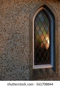 Leaded diamond pattern stained glass church window at sunset, orange, green, brown, blue with light reflections
