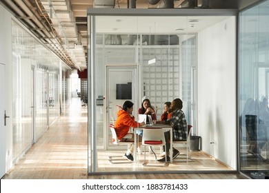 Leader Of The Students Team Talking At Group Office Meeting Sitting At Conference Table At The Separate Isolated Room Behind Glass Door. Team Of People Listening To Coach Or Leader Teaching And