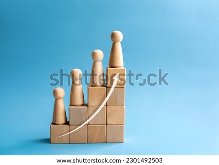 Leadership with business success concept. Modern rising up arrow and wooden figures standing on a growth graph chart steps arranged by wood cube blocks isolated on blue background with copy space.