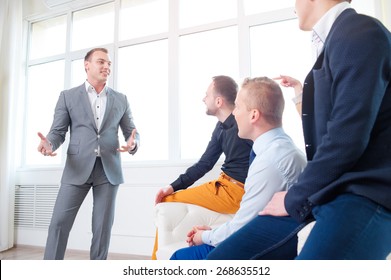 Leadership And Charisma. Business Speech. Handsome Young Man In Grey Suit Talking To His Colleagues - Group Of Young People.