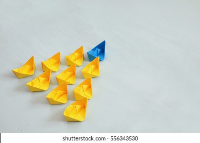 Leadership concept with paper boats on blue wooden background. One leader ship leads other ships. Filtered and toned image