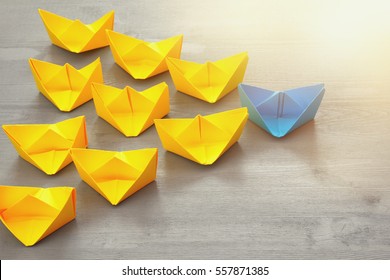 Leadership concept with paper boats on blue wooden background. One leader ship leads other ships. Filtered and toned image - Shutterstock ID 557871385