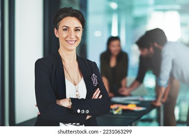 Leading a company that stands by being bold. Portrait of a businesswoman standing in an office with her colleagues in the background. - Shutterstock ID 2231063299