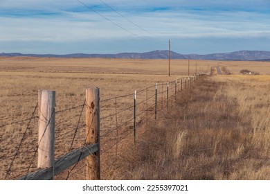 Leading lines along barb wire fence leading to winding country road surrounded by yellow grass pasture with mountain range in distance of rural New Mexico - Powered by Shutterstock