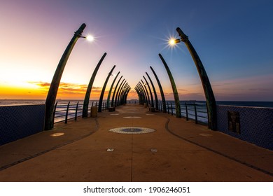 Leading lines view of a unique pier, looking towards the ocean at sunrise - located in Umhlanga Rocks, South Africa. No people visible.