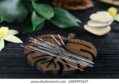 Leaf shaped coaster with acupuncture needles on black wooden table