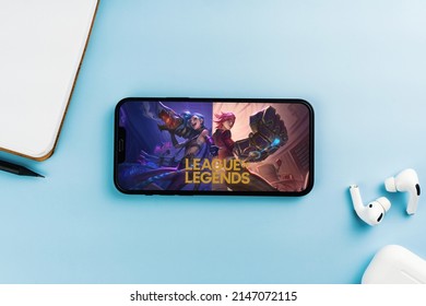 League of Legends (LOL) mobile game app on the smartphone screen. Blue background with notepad and AirPods. Rio de Janeiro, RJ, Brazil. April 2022.