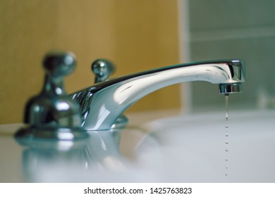 Leaky bathroom faucet, closeup with bokeh background.