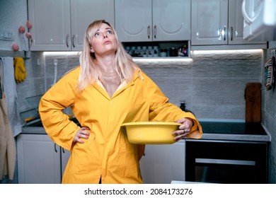 Leaky Pipe In The Ceiling. Woman In Yellow Raincoat Looking Up At Water Leak. Frustrated Female At Home Flooded By Upstairs Or Roof Damage 