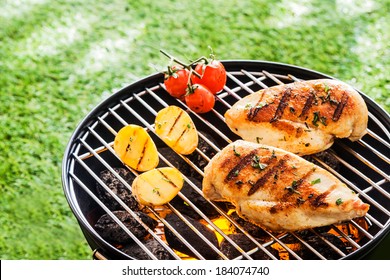 Lean Healthy Chicken Breasts Grilling Over The Hot Coals On A Portable BBQ With Fresh Tomatoes And Potatoes For A Healthy Low Fat Meal