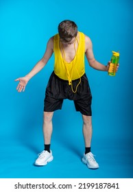 Lean Sportsman In A Yellow T-shirt And Black Shorts On A Blue Background. A Funny Sportsman With A Yellow Bottle Of Water And A Yellow Jump Rope Looks Down At His Feet. Bad Workout