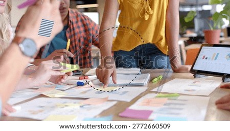 Leaning team of five collaborating at table in office, showing mustard top, tablet and sticky notes. Collaboration, brainstorming, planning, analytics, charts, data, workspace