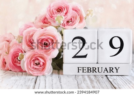 Leap year.  White wood calendar blocks with the date February 29th and pink ranunculus flowers over a wooden table. Selective focus with blurred background. 