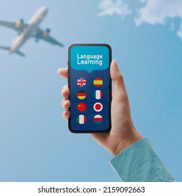 Learn Languages Online: Hand Holding A Smartphone With Language Learning App And Set Of Flags