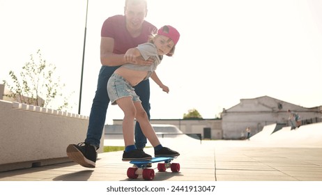 learn to skateboard. dad teaches daughter to ride a skateboard outdoors at playground. father and daughter play training concept. lifestyle parent teaching child daughter to skateboard - Powered by Shutterstock