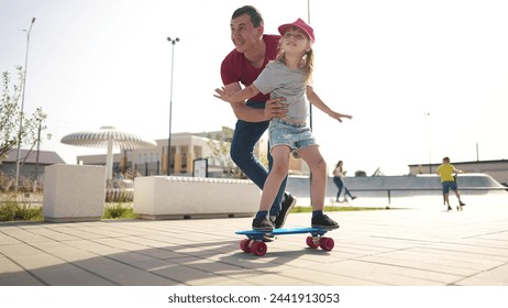 learn to skateboard. dad teaches daughter to ride a skateboard outdoors at playground. father and daughter play training concept. parent teaching child daughter to lifestyle skateboard - Powered by Shutterstock