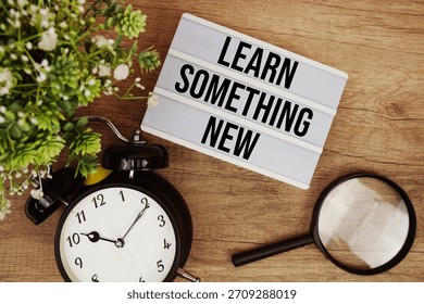 Learn Something New text in lightbox with magnifying glass and alarm clock flat lay on wooden background