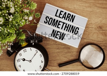 Learn Something New text in lightbox with magnifying glass and alarm clock flat lay on wooden background