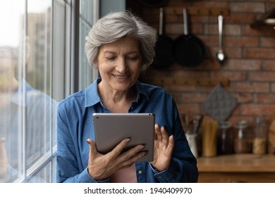 Learn using gadgets. Active smiling middle aged latin female pensioner use modern tablet computer at kitchen. Happy mature grandmother hold digital pad search information online read electronic book