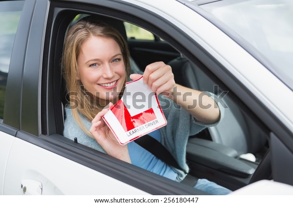 Learner\
driver smiling and tearing l plate in her\
car