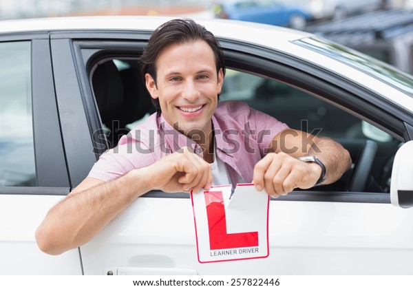 Learner\
driver smiling and tearing l plate in his\
car
