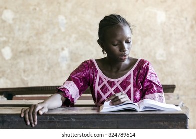 Learning Activity Symbol: Young African Girl Sitting In Classroom Reading A Book. Education Symbol For Africa. Single Person Studying Learning Her Lesson.