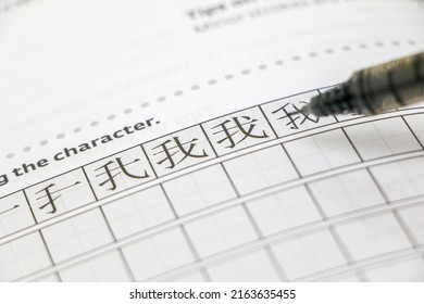 Learning Chinese concept, learning how to write simplified Chinese characters, pen over tianzi ge grid paper, practicing writing 我 meaning ‘I’ or ‘me’ in Chinese