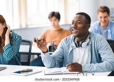 Learning Concept. Portrait of interested African American guy sitting at table with multi ethnic classmates, talking to teacher, asking or answering question, discussing new theme, topic or theory