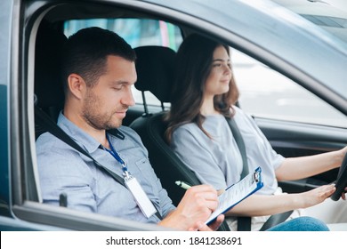 Learning to drive a car. Male instructor and female student practicing in driving. Young man notice results of test in his paper. Cheerful woman satisfied with driving lessons. - Shutterstock ID 1841238691