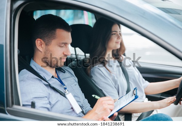 Learning to drive a\
car. Male instructor and female student practicing in driving.\
Young man notice results of test in his paper. Cheerful woman\
satisfied with driving\
lessons.