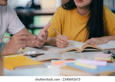 Learning, Education And School Concept. Young Woman And Man Studying For A Test Or An Exam. Tutor Books With Friends. Young Students Campus Helps Friend Catching Up And Learning.