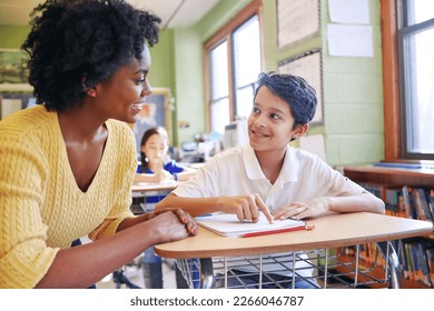 Learning, education and teacher help student with assignment in elementary school. Classroom support, scholarship and happy black woman or educator aid, explaining or helping male learner in class. - Powered by Shutterstock