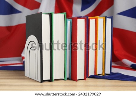 Learning foreign language. Different books on wooden table near flag of United Kingdom