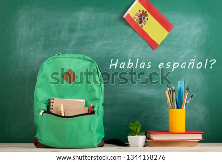 Learning languages concept - green backpack, blackboard with text 