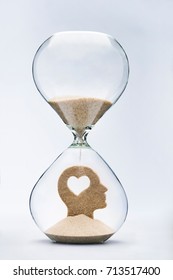 Learning to love concept, with falling sand taking the shape of a cut out heart inside a human head, inside a hourglass