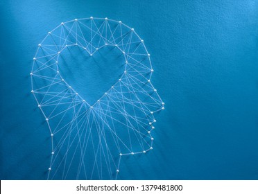 Learning to love concept. Network of pins and threads in the shape of a cut out heart inside a human head symbolising that love is the core of our being and has its own logic.
