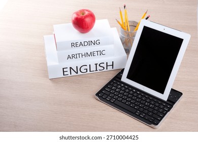 Learning materials and tools arranged on a desk with books, an apple, and a tablet keyboard