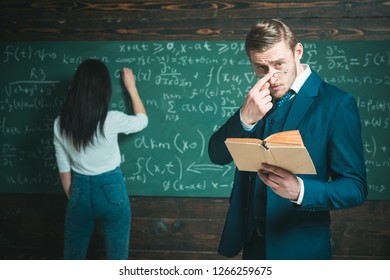 Learning math enables me to think clearly. Teacher man in glasses read problem statement from textbook to girl student. Rear view woman write equation on chalkboard. Doing sums. School day.