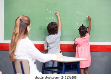 Learning mathematics at elementary school. Multi ethnic students writing on chalkboard with teacher observing. - Powered by Shutterstock