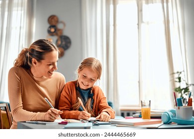 Learning new together. Two generations of optimistic females sitting at corner of desktop and writing in copybooks. Easygoing lady looking at kid doing exercises and pretending practising same task. - Powered by Shutterstock