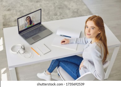 Learning online education. Red-haired girl in glasses studying using a laptop video call chat web camera watching video course college university sitting in a chair at home. 