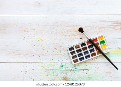 Learning painting concept  paint brush   box and watercolors white wooden table and splashes  artistic background  creative art workplace for children kids  top view and copy space  flat lay