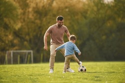 Learning To Play Soccer. Happy Father With Son Are Having Fun On The Field At Summertime.