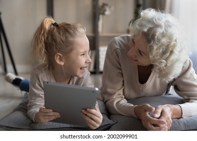 Learning And Playing. Older Grandmother Study Maths Or English With Little Preteen Grandkid Using Modern Tech. Aged Nanny And Gen Z Girl Lying On Pillows Watch Video In Education App On Digital Tablet