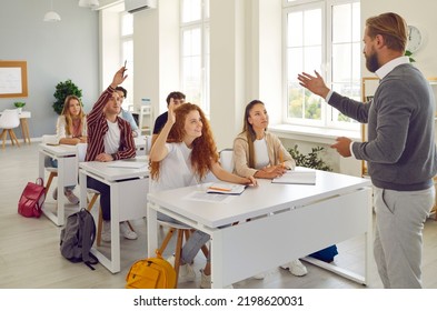 Learning process. Active college students raise their hands in class to answer teacher's questions. College or high school students sit at class desks and interact with male teacher. - Powered by Shutterstock