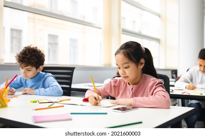 Learning Process Concept. Portrait of Small Schoolchildren Smiling, Sitting At Desk Taking Notes And Writing in Exercise Copybook. Junior Classroom with Diverse Group of Children Learning New Stuff - Powered by Shutterstock