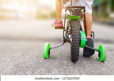 Learning To Ride A Bike Concept, The Little Boy Is Practicing Cycling A Bicycle With The Training Wheels On The Road.