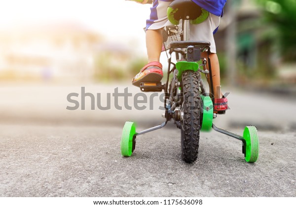 Learning to\
ride a bike concept, The little boy is practicing cycling a bicycle\
with the training wheels on the\
road.